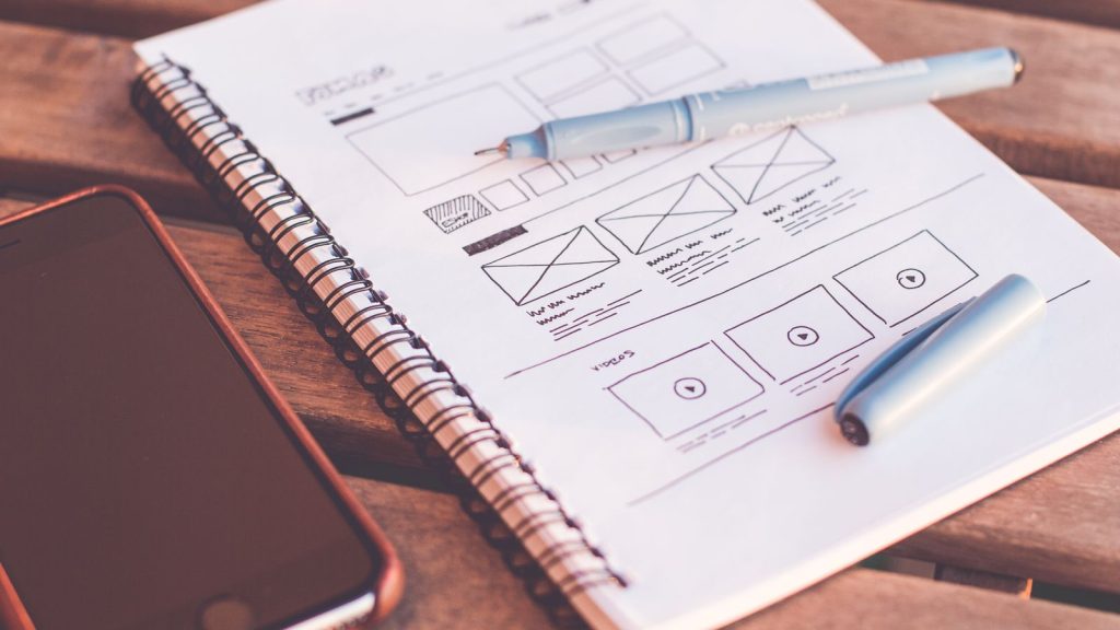 Wireframe d’interface dessiné à la main sur un carnet à côté d’un téléphone